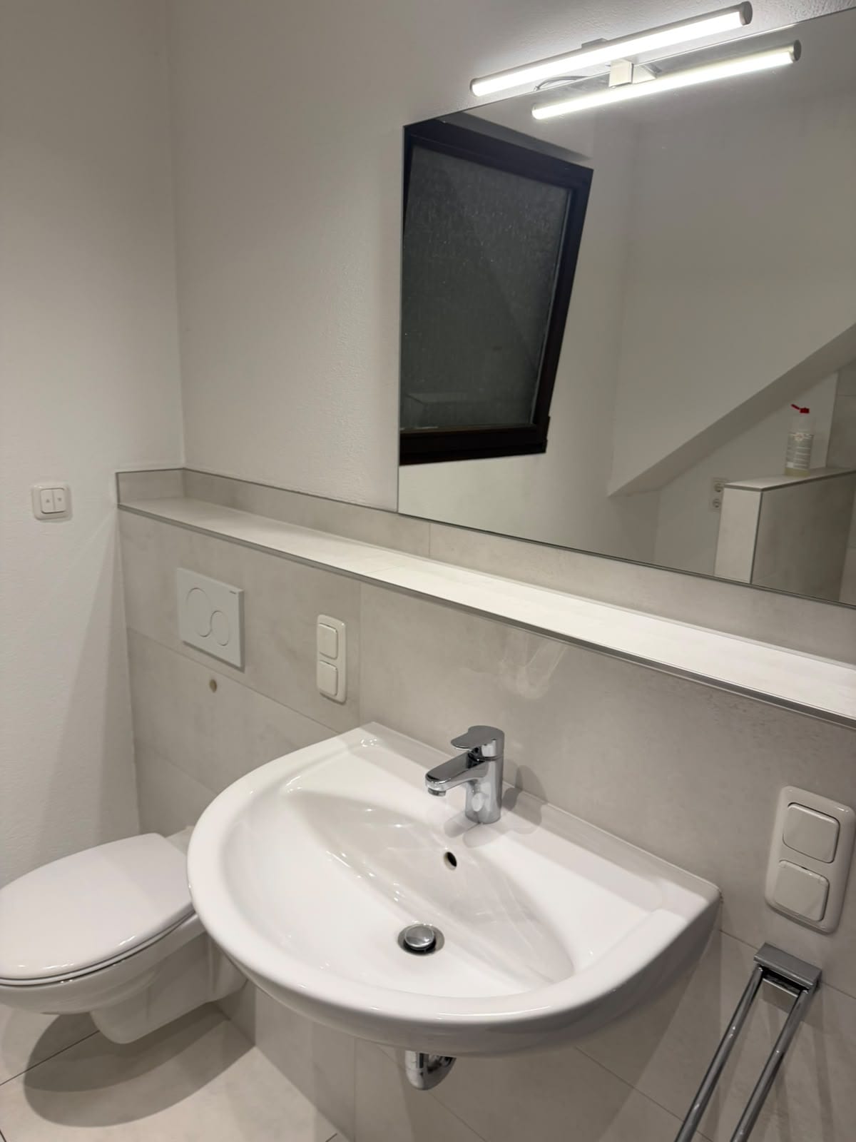 Sauberes Bad mit Waschbecken, Hänge-WC, Spiegel und Ablage unter der Dachschräge