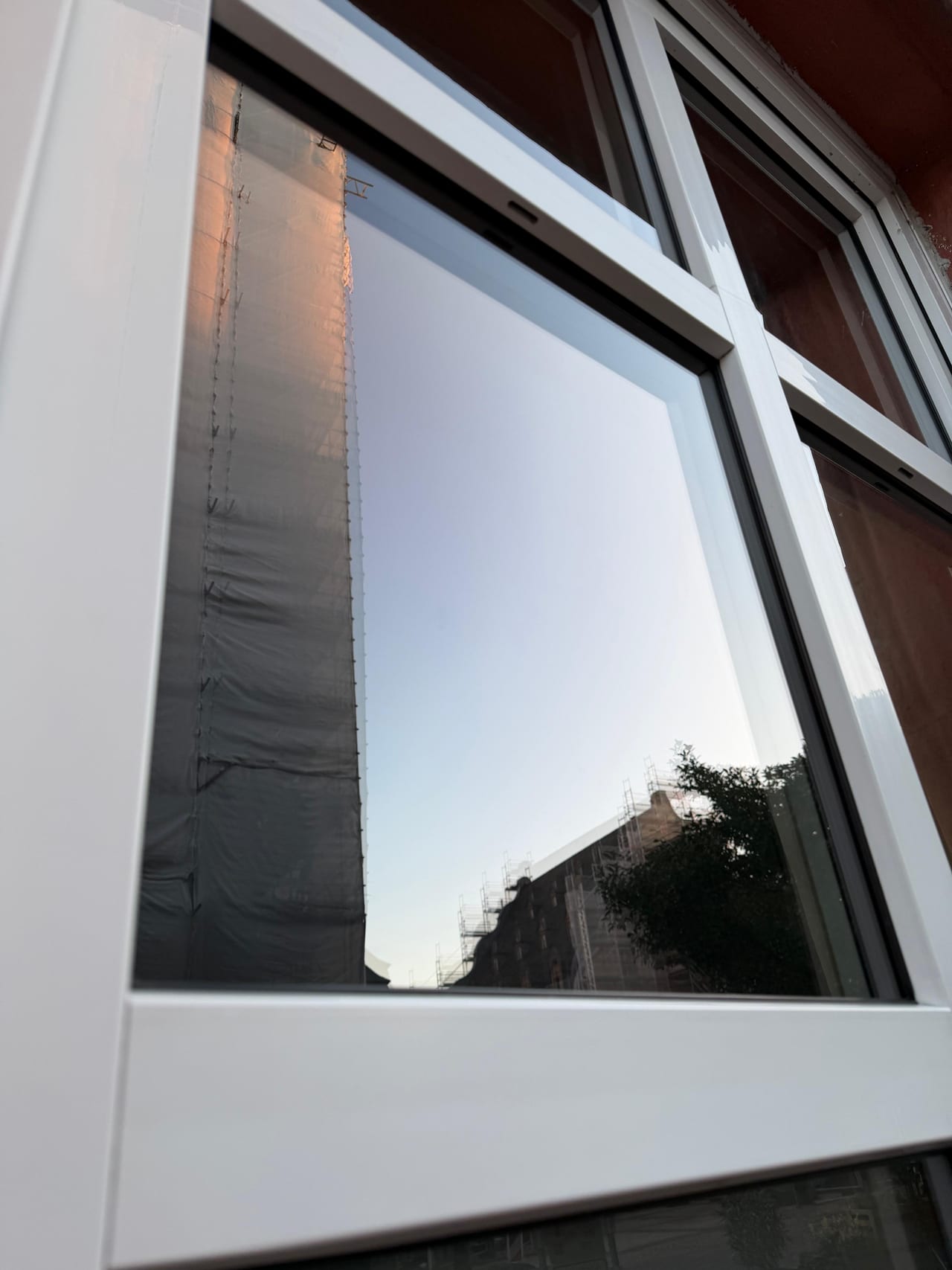 Nahaufnahme einer Fensterscheibe mit weißem Rahmen und Spiegelung des Himmels